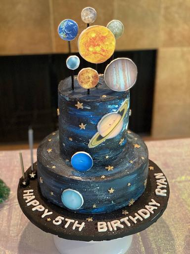 Galaxy-themed birthday cake decorated with edible luster dust, giving a shimmering, metallic finish to the cosmic design. Featuring planets, stars, and a deep space effect, this cake celebrates Ryan's 5th birthday with a dazzling, celestial touch.