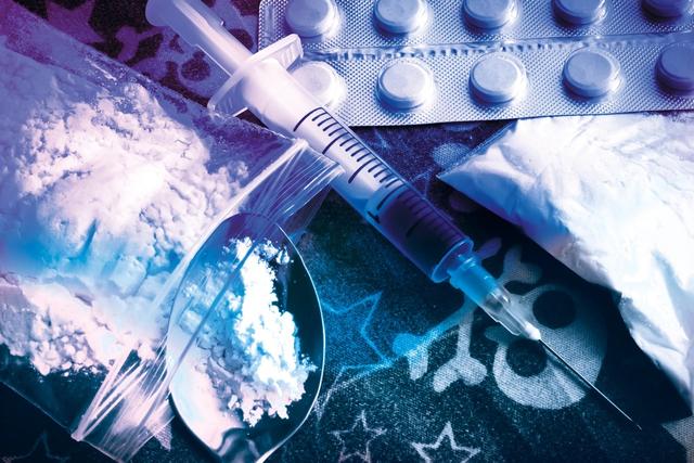 Illicit drug paraphernalia with syringe, powder-filled bags, spoon, and blister-pack pills—visual of synthetic drug use, overdose risk, and polydrug contamination
