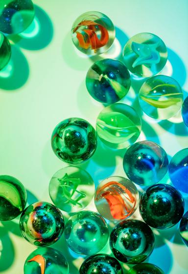 Close-up of colorful glass marbles on a green and blue gradient background, showcasing their vibrant patterns and reflective surfaces