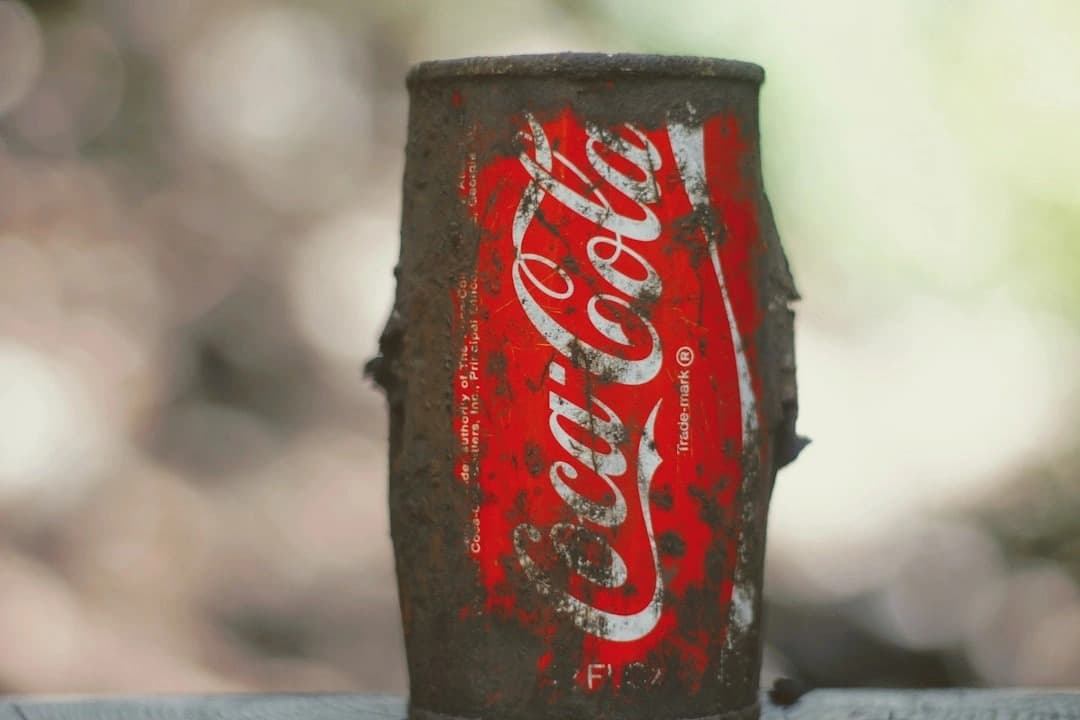 Close-up of a damaged Coca-Cola soda can on a wooden ledge, illustrating contamination risk amid the breaking recall of Coca-Cola Zero and Classic cans for potential metal fragments